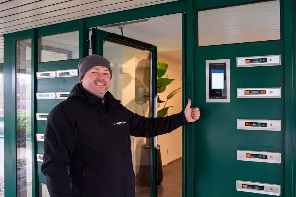 Monteur van Intercom-Lease bij een groene entreedeur met Akuvox-buitenpost met codeklavier in RVS-inbouw (impressie)