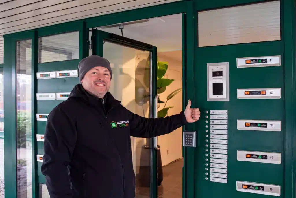 Monteur van Intercom-Lease bij een intercompaneel naast een groene entreedeur